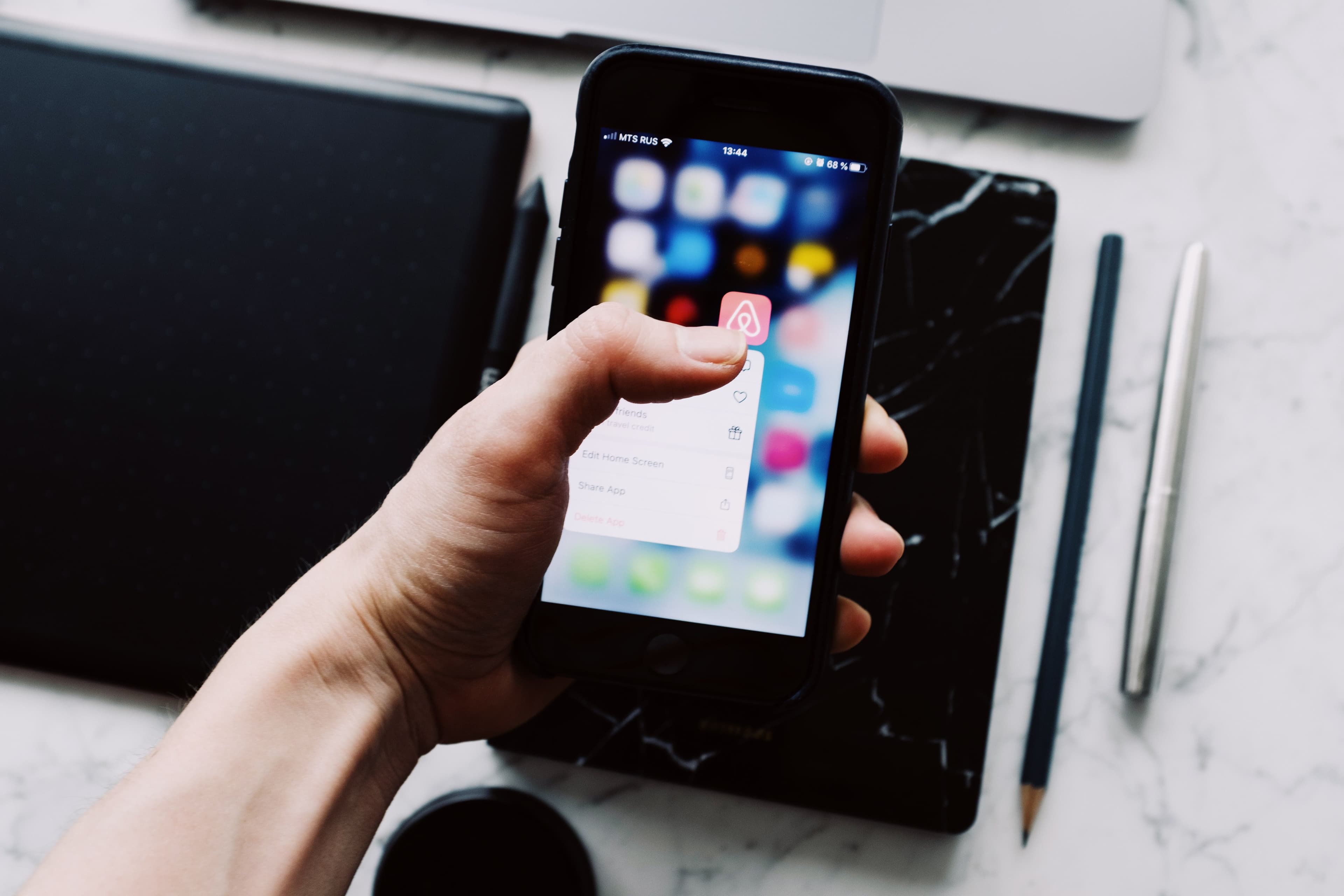 Pessoa segurando um smartphone com ícones de aplicativos sobre a mesa
